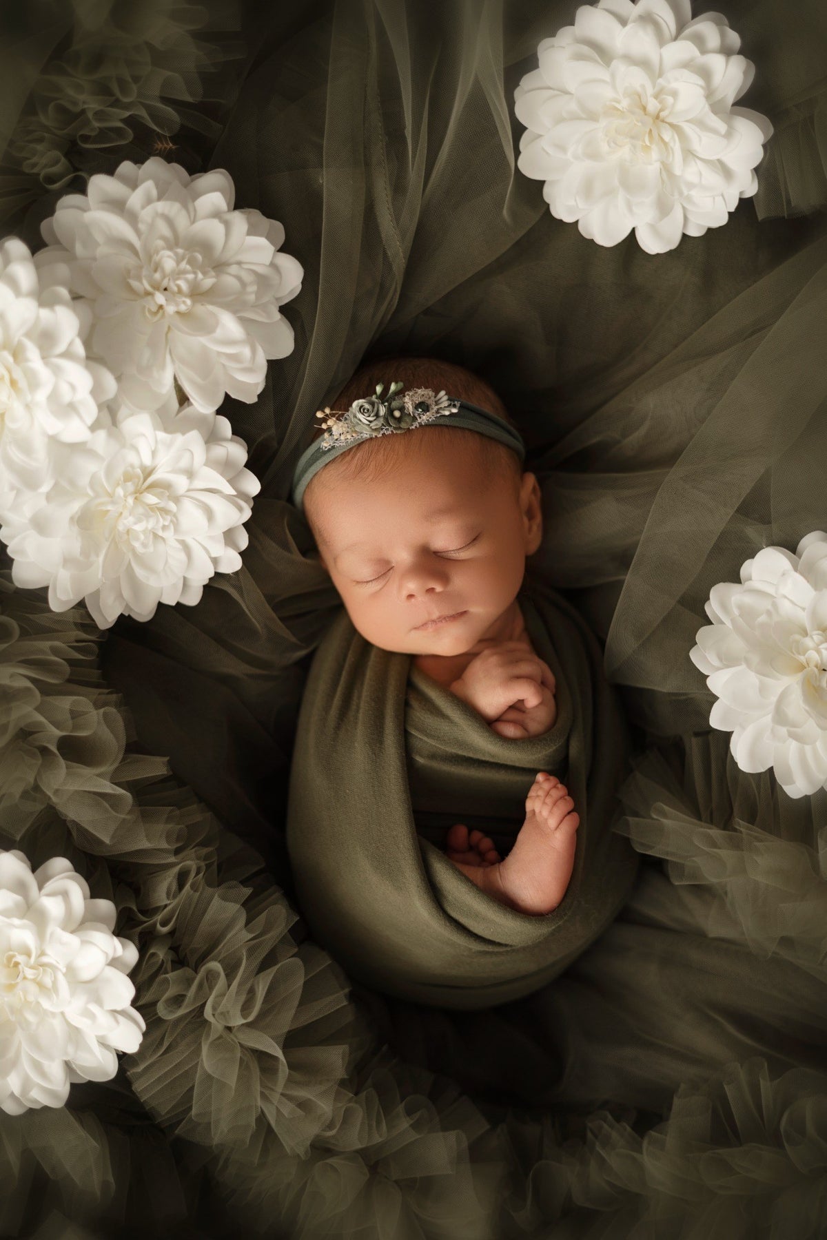 Bébé emmailloté en vert entouré de grandes fleurs blanches