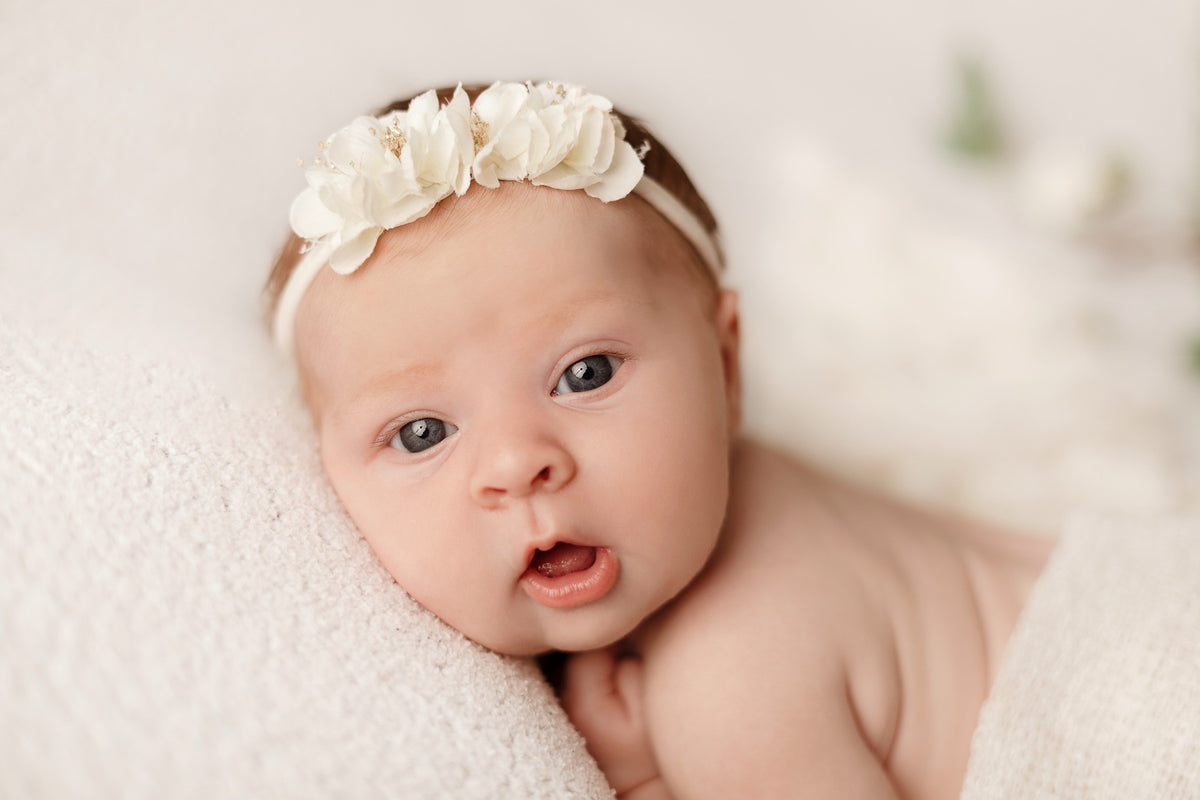 Portrait rapproché d’un bébé avec bandeau de fleurs blanches