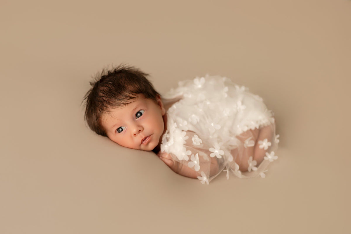 Nouveau-né photographié éveillé dans un décor blanc et délicat