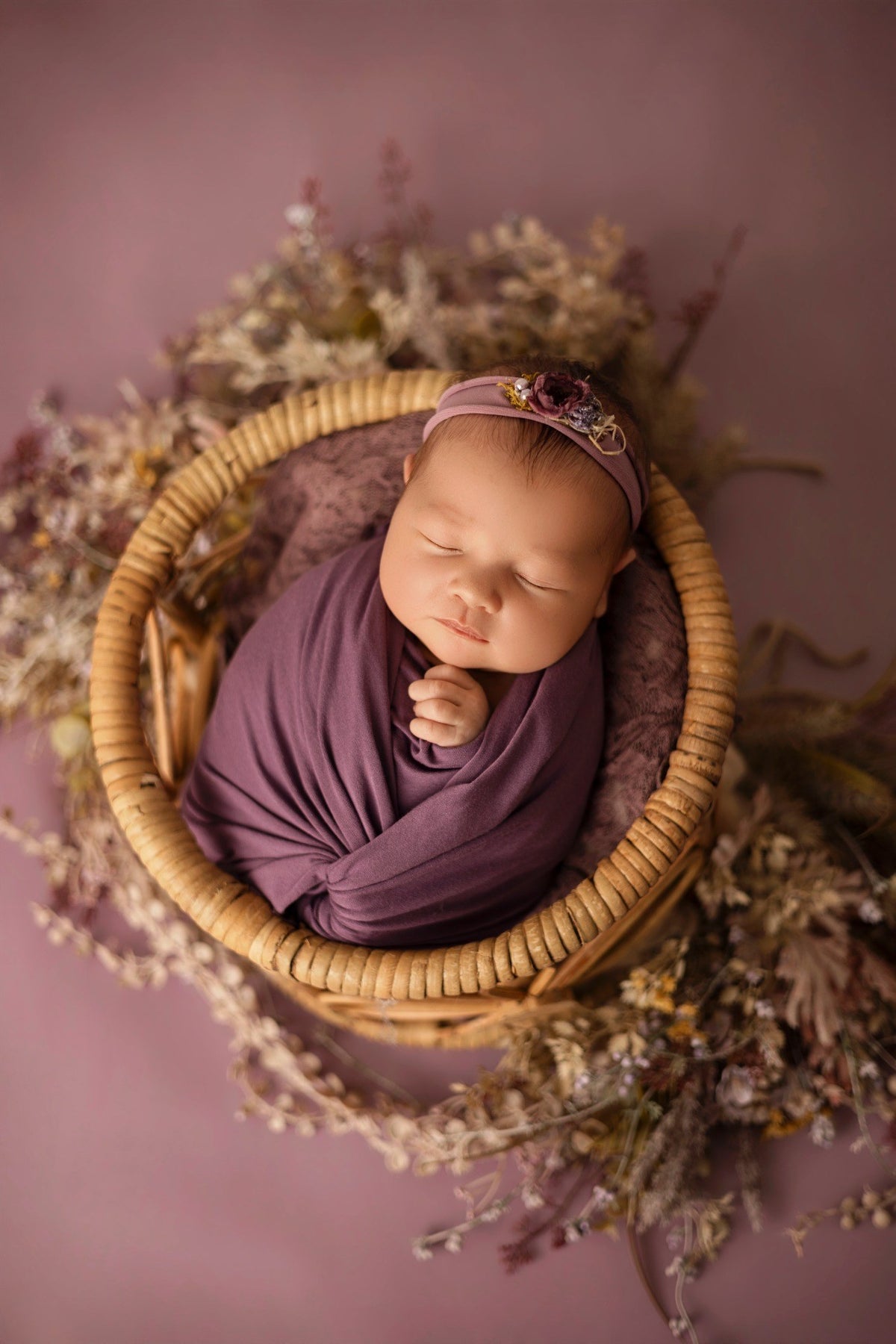 Nouveau-né emmailloté dans un panier et décor violet fleuri
